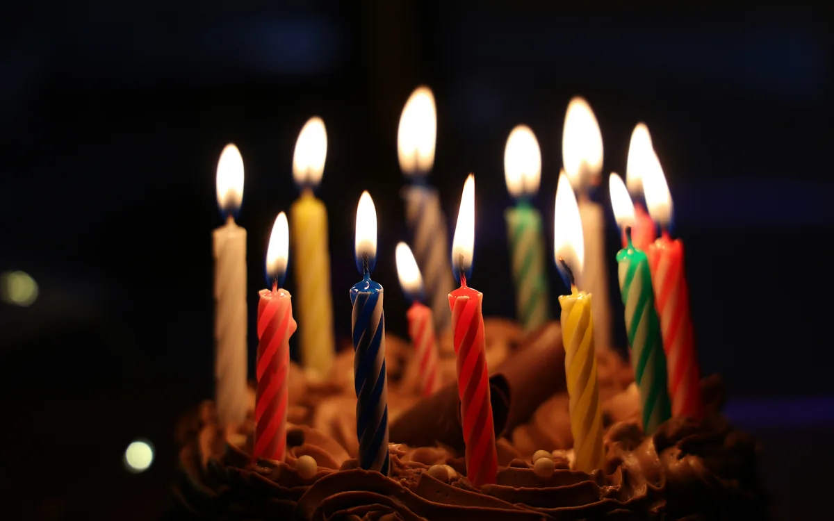 Lit birthday candles glowing on a chocolate celebration cake against a dark background.