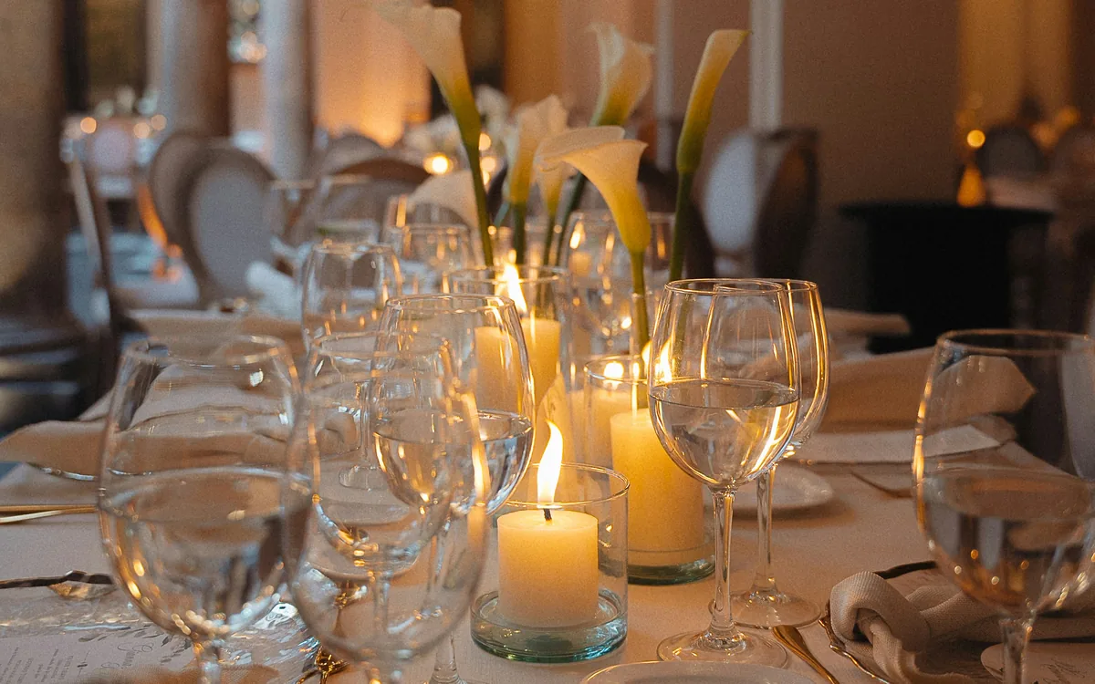 A candlelit private dinner table set with wine glasses, white calla lilies and warm candlelight.